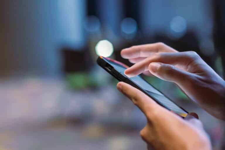 Hands holding a smartphone and typing on the screen with a blurred outdoor background.